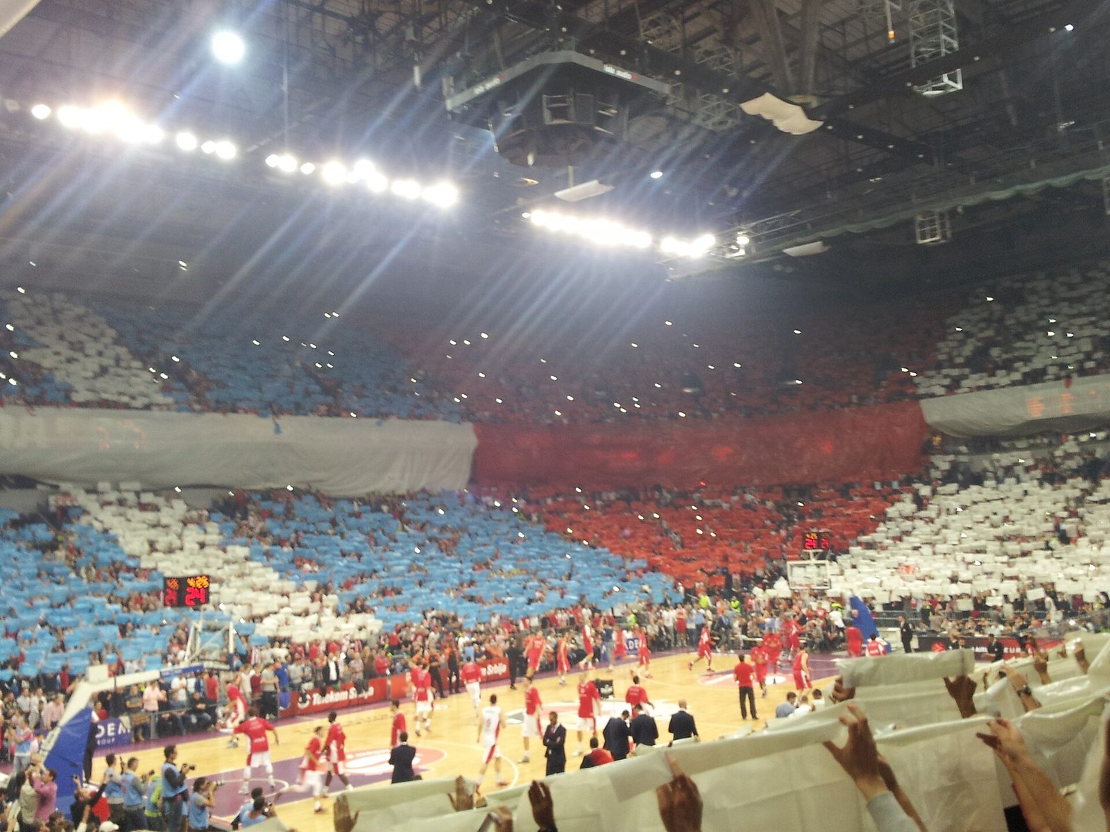 Inside Belgrade Arena during a Crvena Zvezda home game, with a red, white and blue card display in the stands